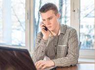 Young man holding phone looking at laptop