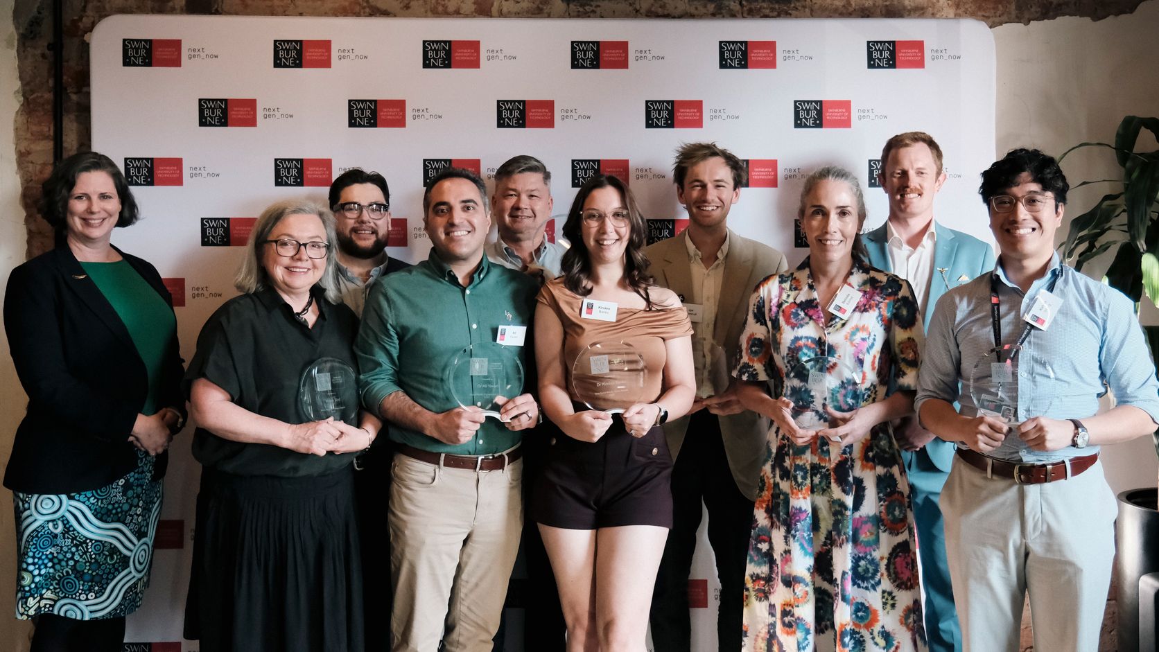 Group of staff hold trophies in front of a Swinburne banner.
