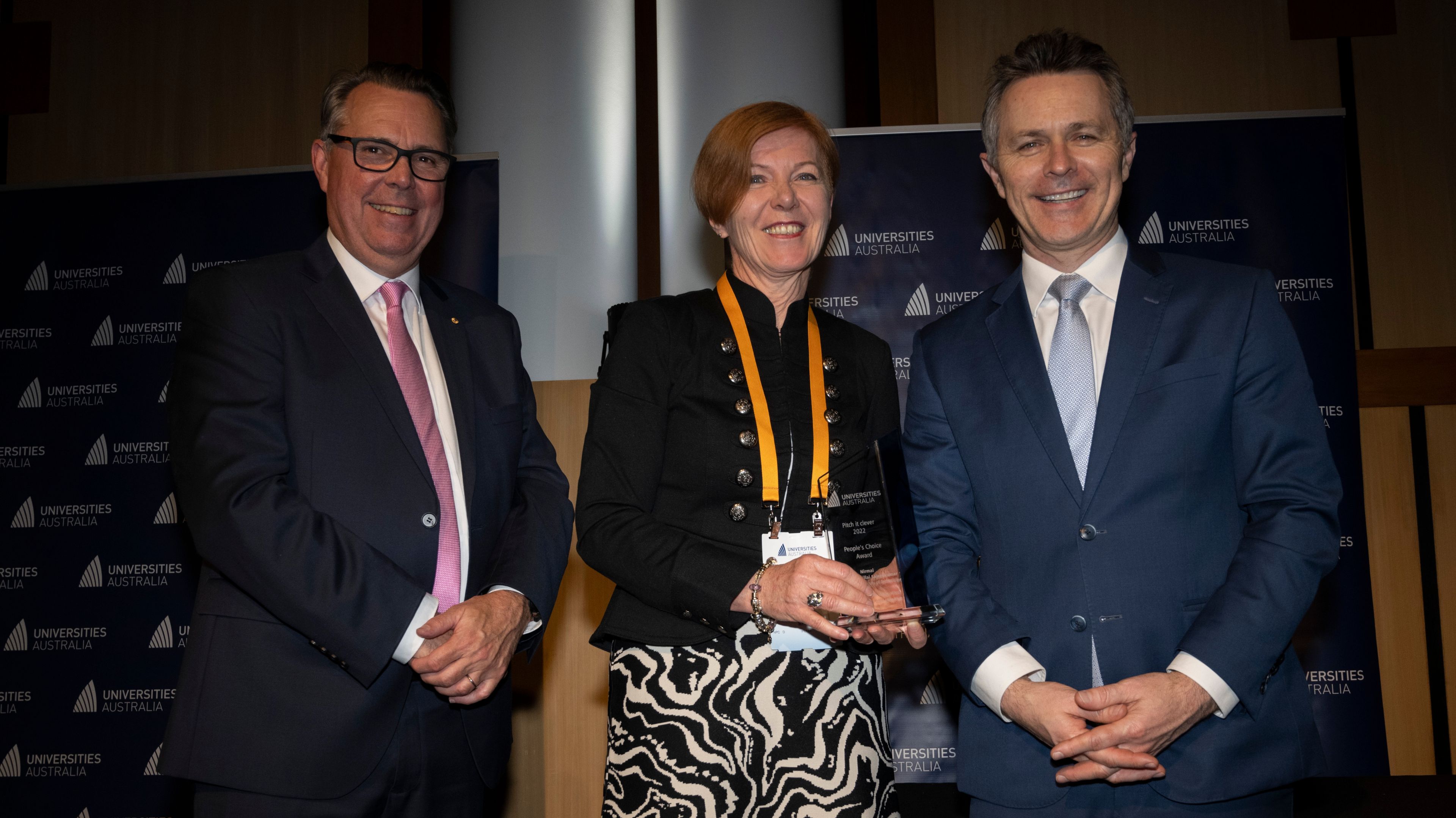 Swinburne Vice-Chancellor Pascal Quester stands smiling with Minister for Education Jason Clare (left) and Professor John Dewar (right). She is holding a glass plaque. 