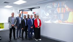 Oracle and Swinburne School of Business, Law, and Entrepreneurship staff celebrating the partnership’s launch at Swinburne's Hawthorn Campus. Eight people all stand together next to a whiteboard with a promotional image displayed  