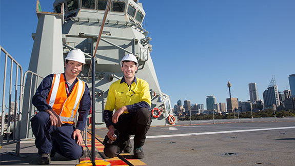Dr Andrew Ang and Matthew Leigh on board HMAS Canberra, kneeling on top deck.