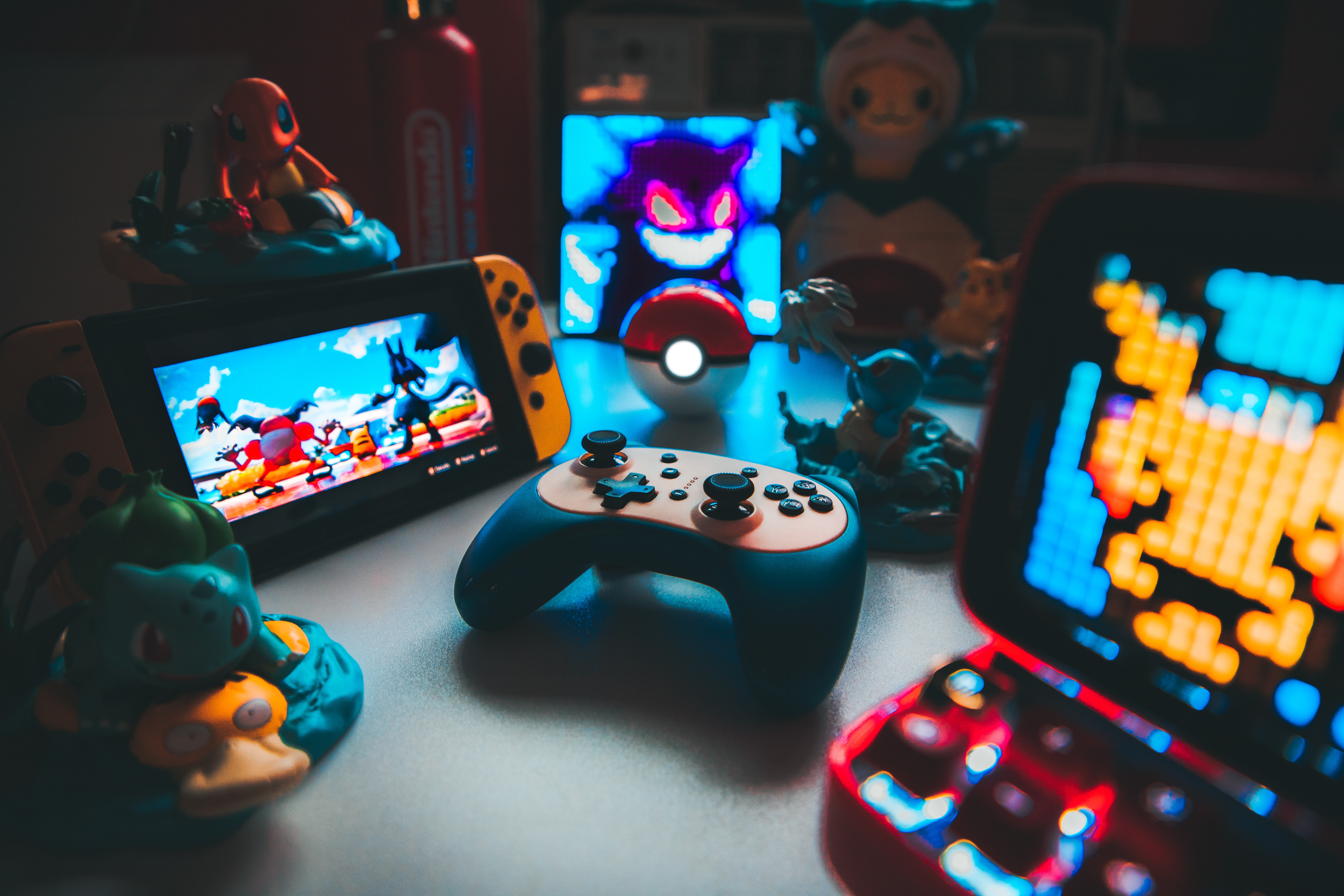 Games paraphernalia on a table - a console in the middle, a Nintendo Switch next to it, both surrounded by Pokemon characters
