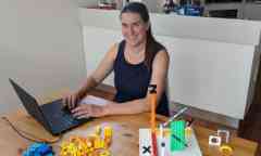 Dr Emily Cook sitting at laptop computer with LEGO construction.