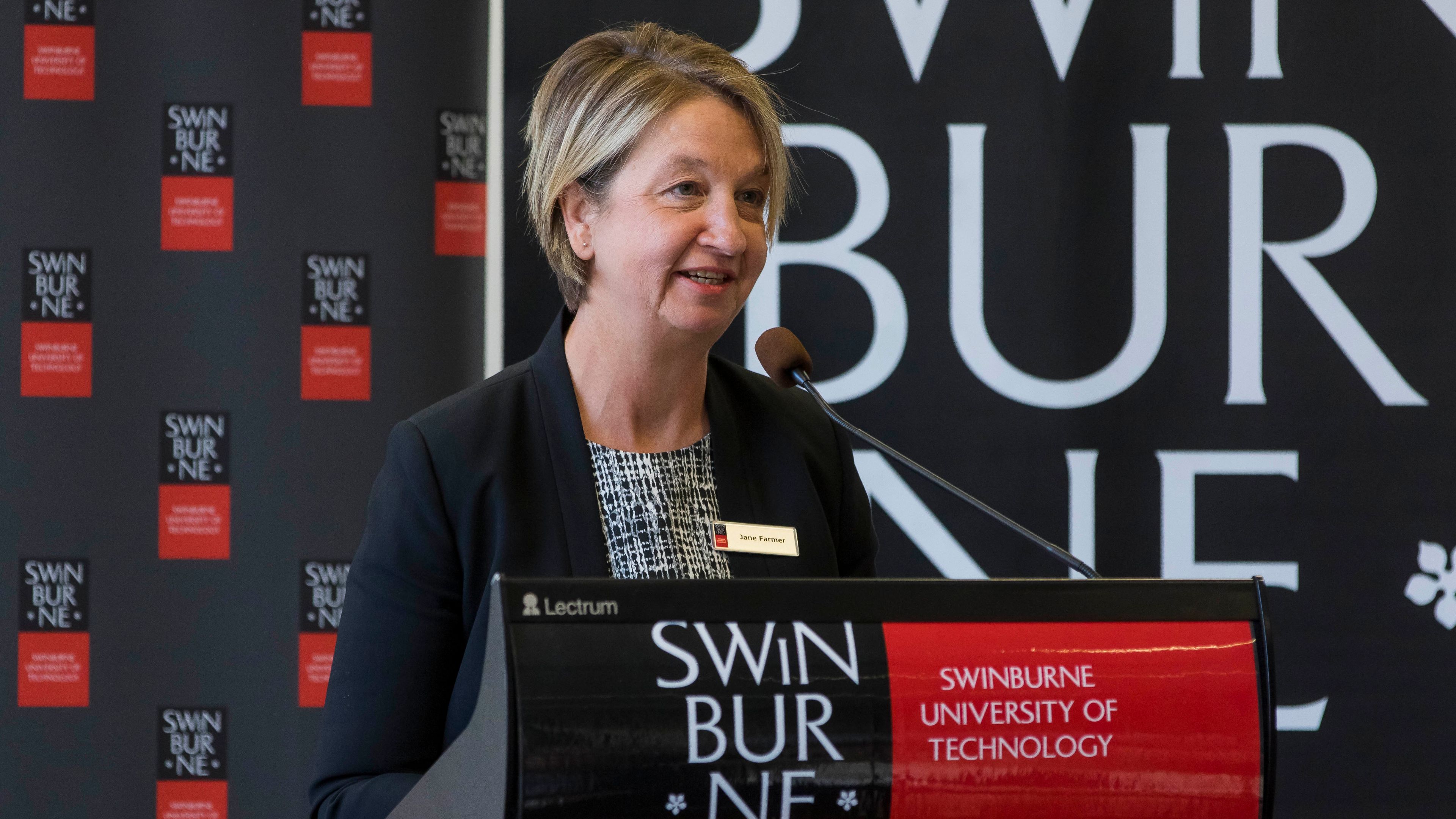 Jane Farmer speaking at a Swinburne branded microphone podium.
