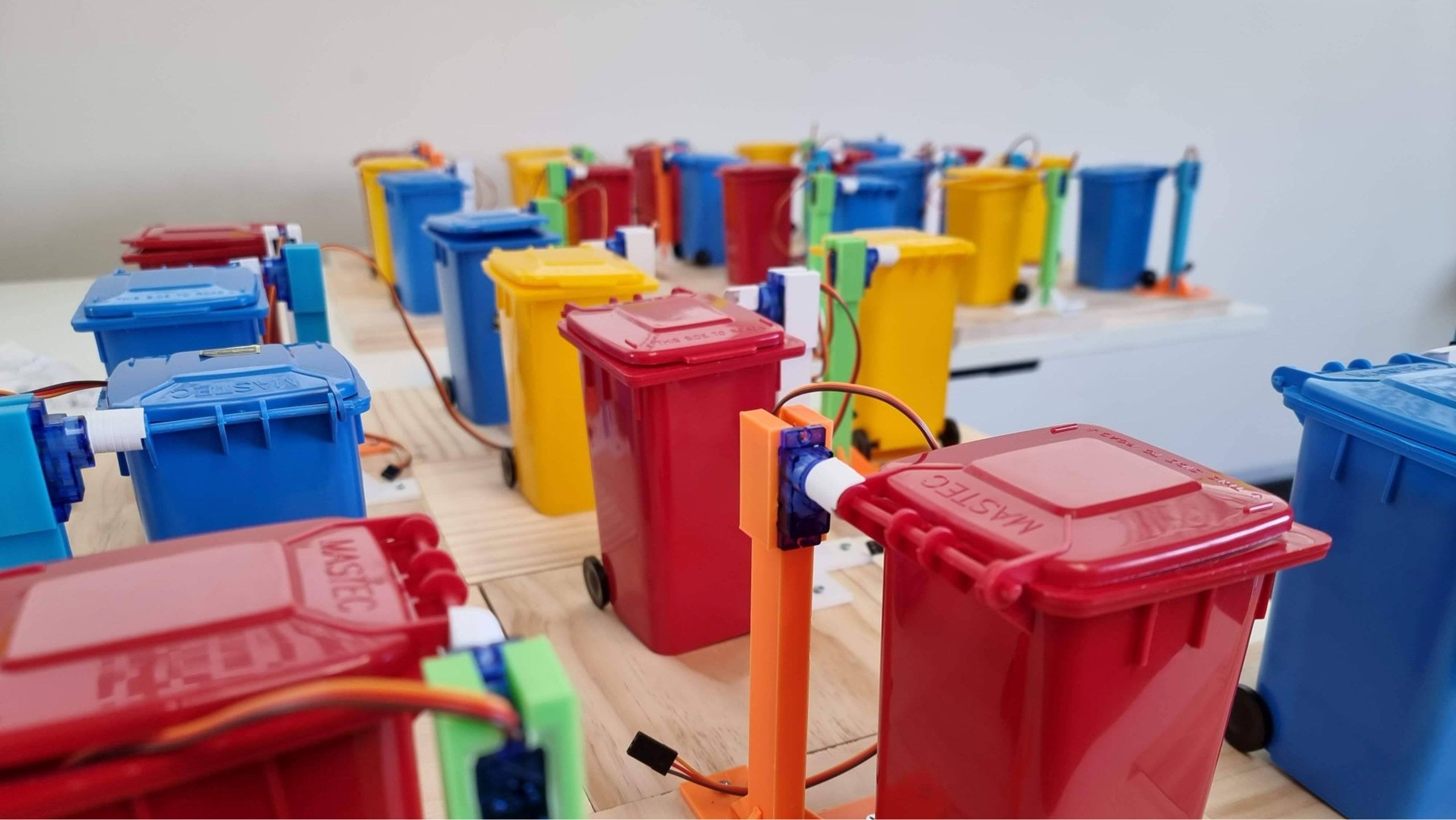 Mini garbage bins in red, blue and yellow are wired with tiny circuits for a KIOSC smart bin project