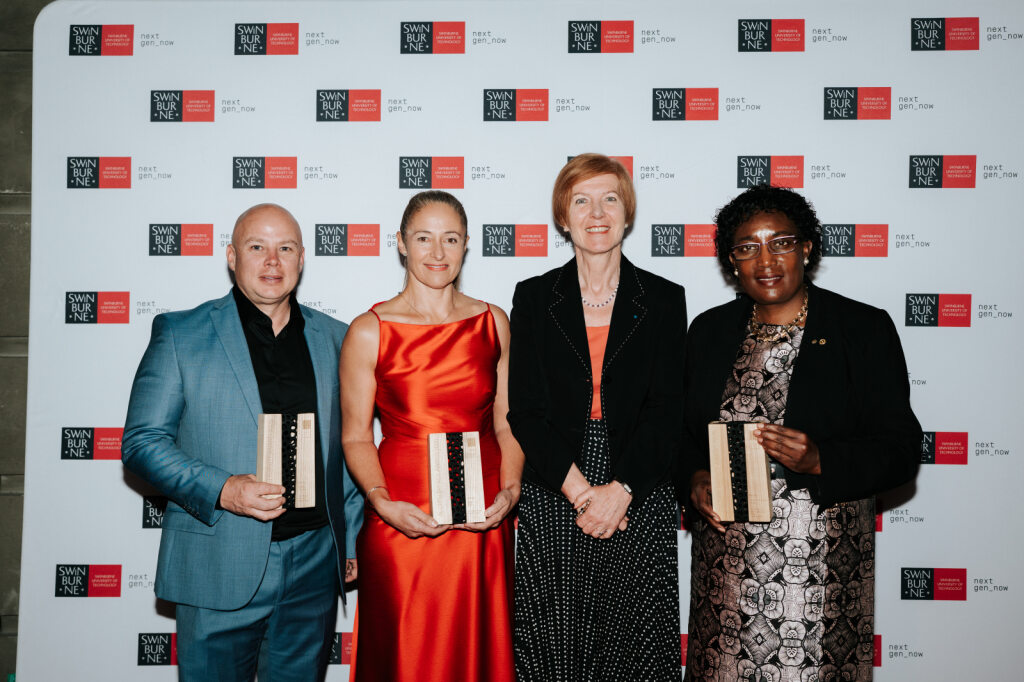 The three AIA event winners stand with Swinburne VC, all smiling. The winners hold trophies 