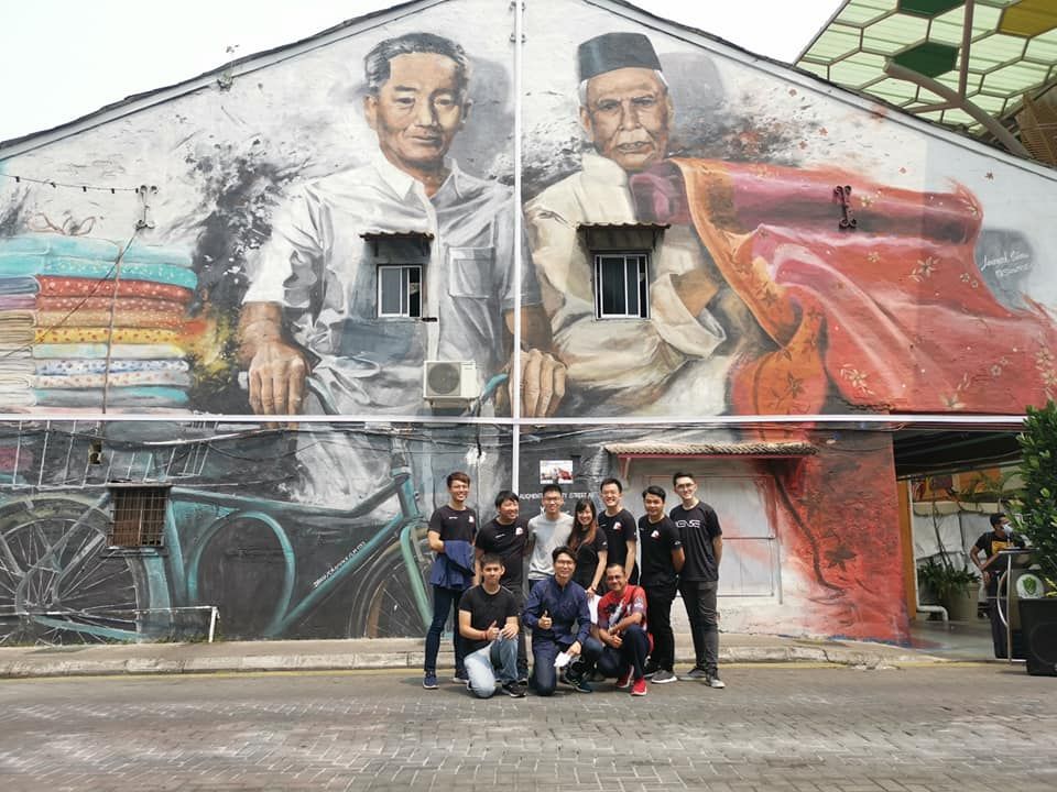 Sarawak alum Lim Jim Hong with a group of his employees from ARx Media by a mural in Sarawak.