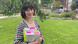 Woman wearing black and white checked top and gold nacklace holds thick law books filled with pink and yellow post it notes