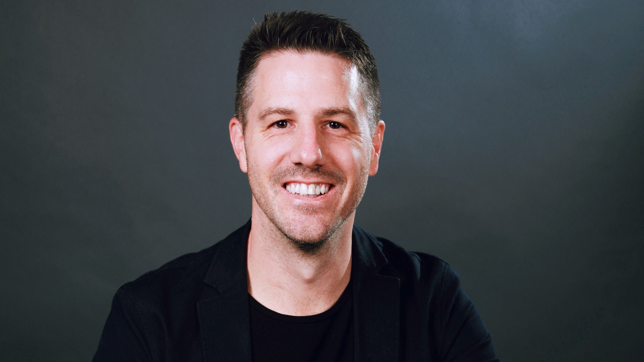 Close up of Andrew Collins smiling to camera with a plain grey background