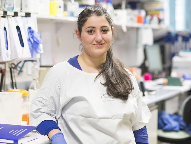 A Swinburne pharmacy placement student wearing a white lab coat and blue gloves, smiles for the camera.