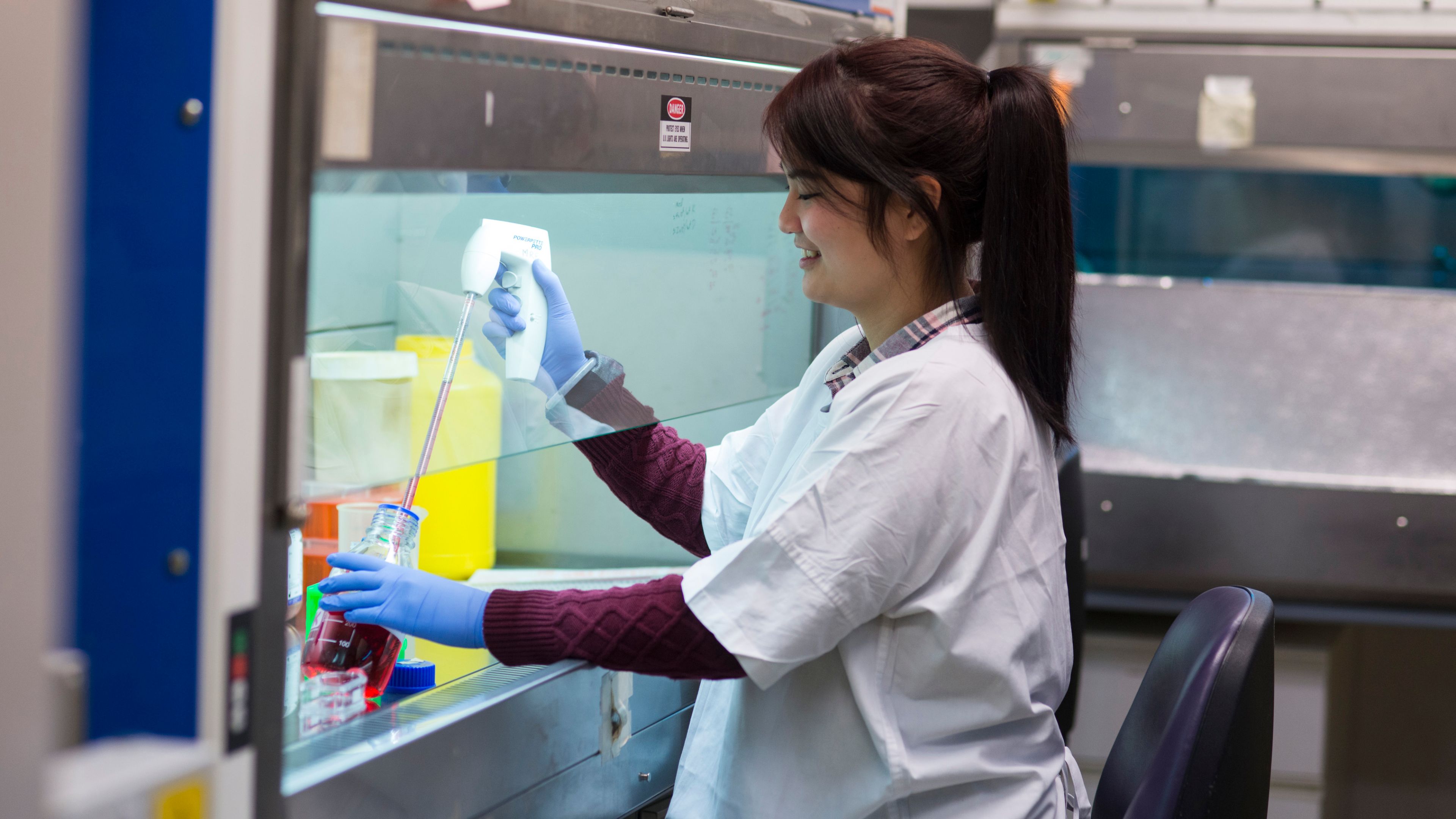 Science student in laboratory using a pipette to extract a liquid from a jar.
