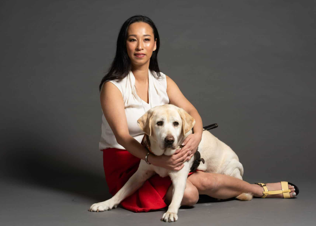 Swinburne alum, Cassandra Chiu, sitting on the floor with her guide dog, Elke, a golden labrador 