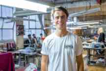 Male student smiles broadly to camera wearing a white top in a workshop