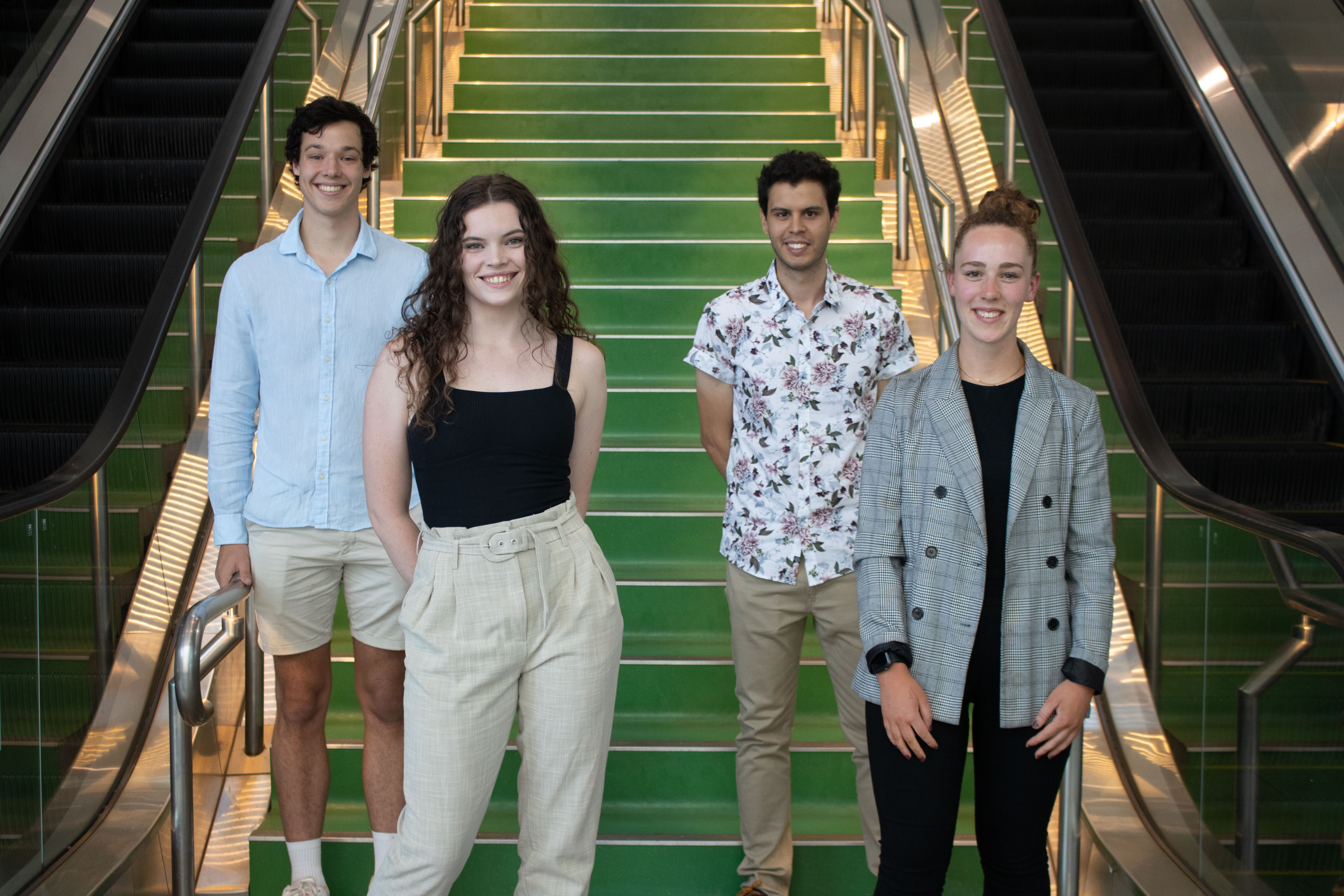 The four recipients stand, smiling, in front of a green set of stairs at Swinburne's AMDC building