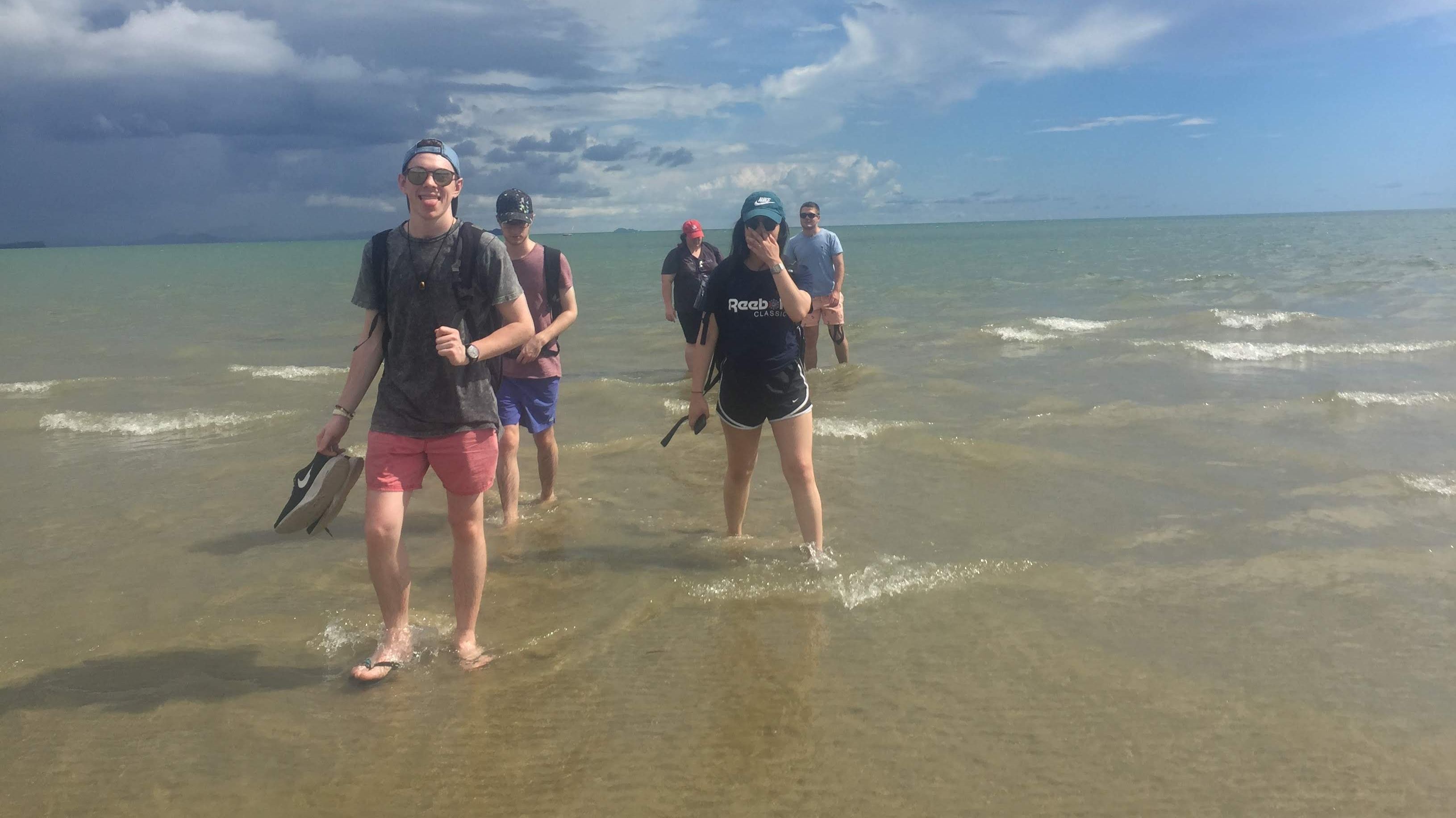 Josh and his friends wading ankle deep through a sunny beach while studying abroad