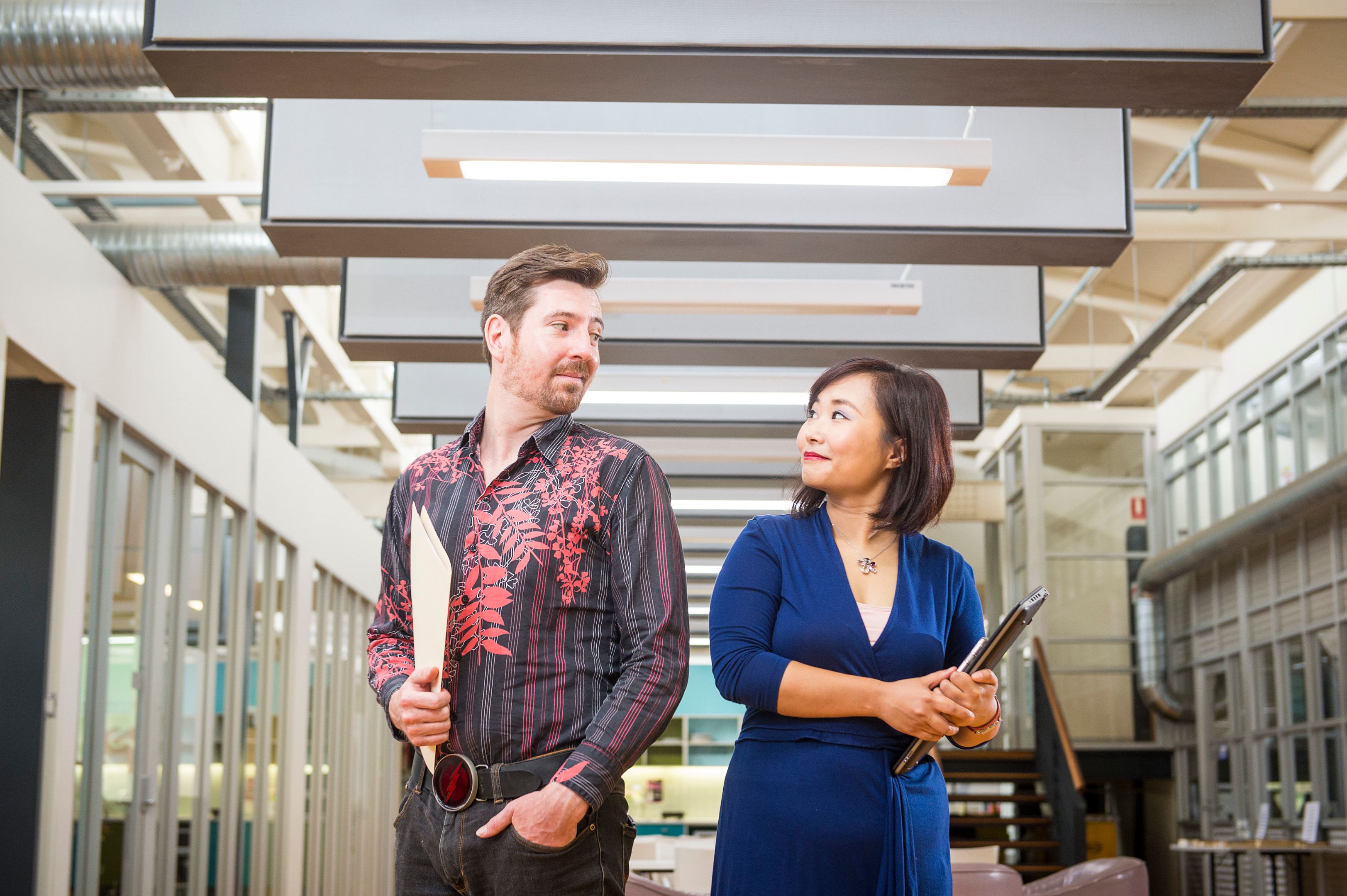 Male and female standing next to each other holding office equipment with their heads turned towards each other