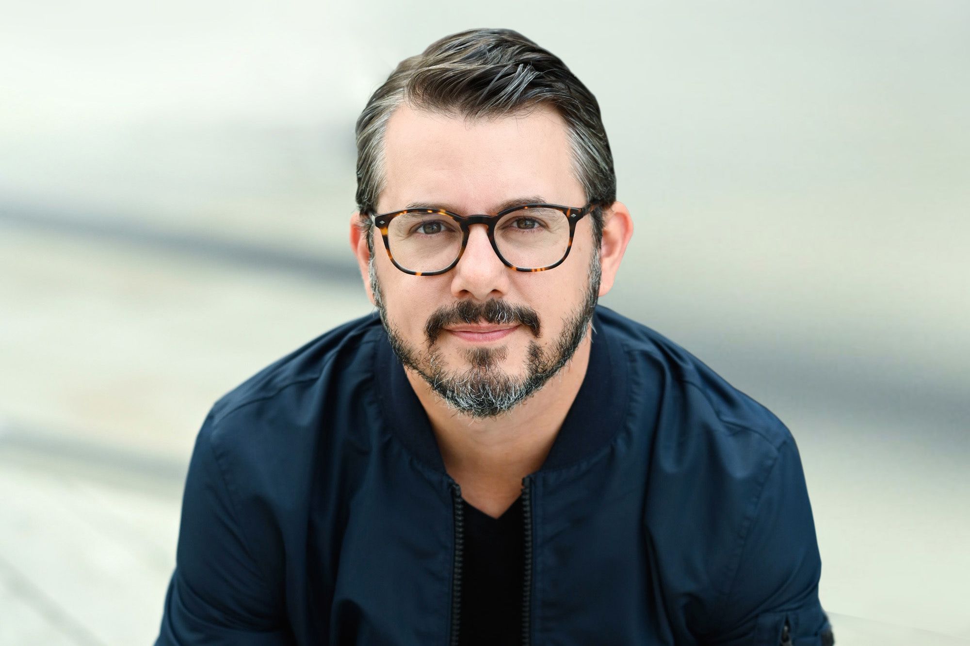 A portrait of Swinburne Master of Entrepreneurship and Innovation alum Michael Giles. He's wearing a navy-blue bomber jacket, tortoiseshell glasses and a focused gleam in his eyes. 