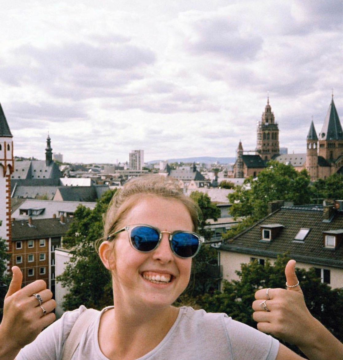 Female smiling at the camera with both thumbs up and the Germany city scape in the background