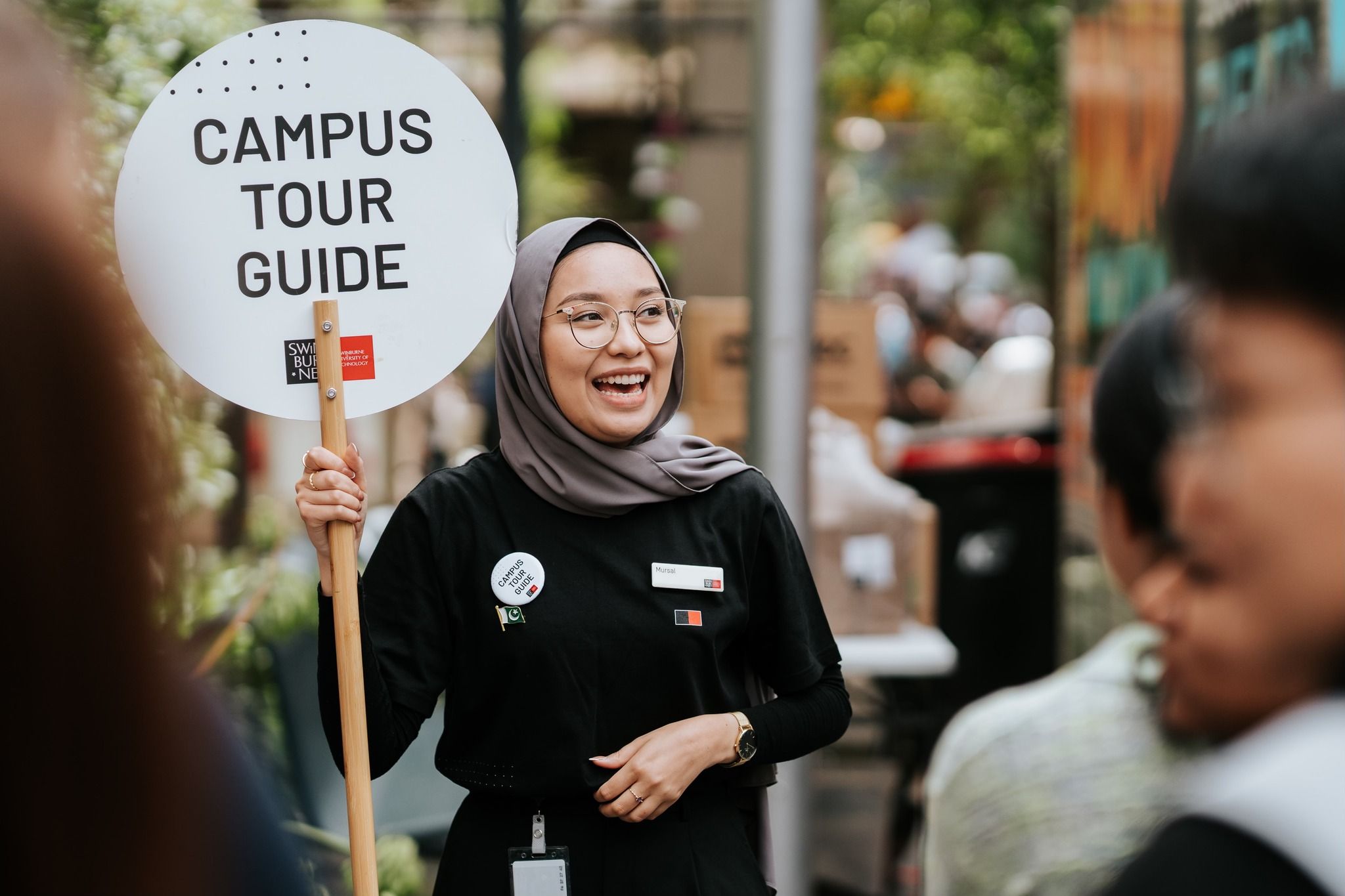 Student holding up a white circular sign on a stick which reads campus tour guide 