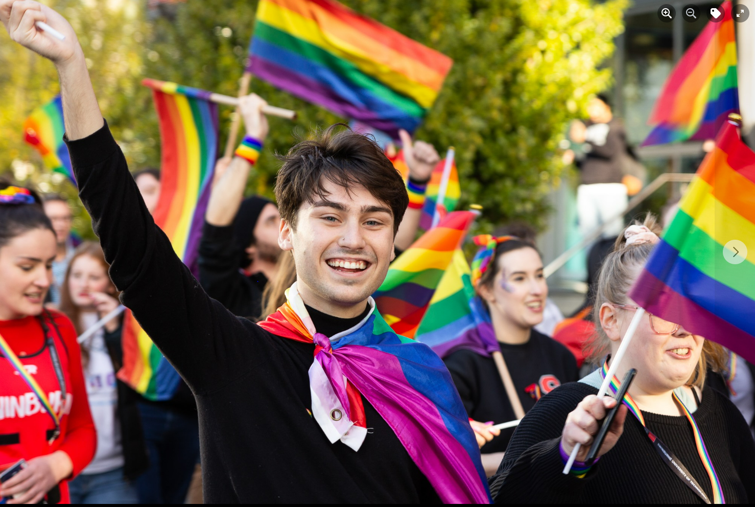 Student wearing long back shirt and wearing rainbow flag tied around his neck 