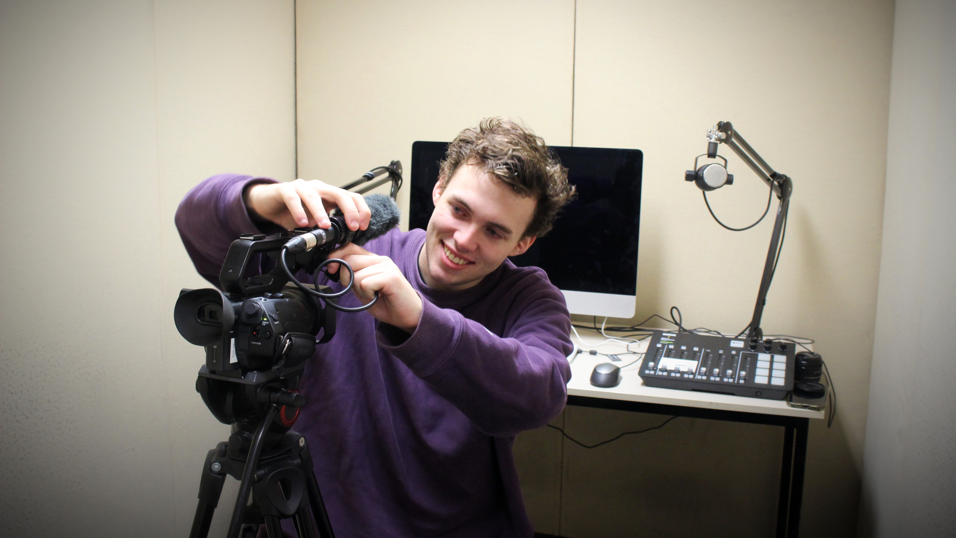 A male student setting up a camera and a microphone in a studio