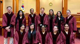 11 students in robes pose in an empty courtroom