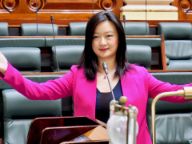 Wesa Chua stands in parliament with her arms stretched out wide and wearing a hot pink jacket