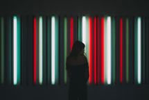 A woman stands in front of a panel of red, white and green vertical neon lights