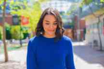 Female student wearing a blue jumper strolling down the street slightly looking down