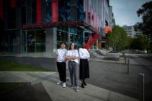 Three Swinburne student ambassadors of varying cultural backgrounds, all aged in their late teens to early twenties, stand proudly out the front of The George building on Swinburne's hawthorn campus