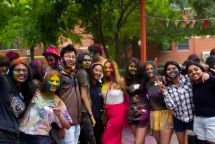 A group of students stand in a row smiling, some with coloured powder on their faces and clothes