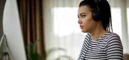 Young girl with dark hair wearing headphones and using a MAC computer 