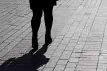 Silhouette of lonely woman walking down the street, black shadow on pavement