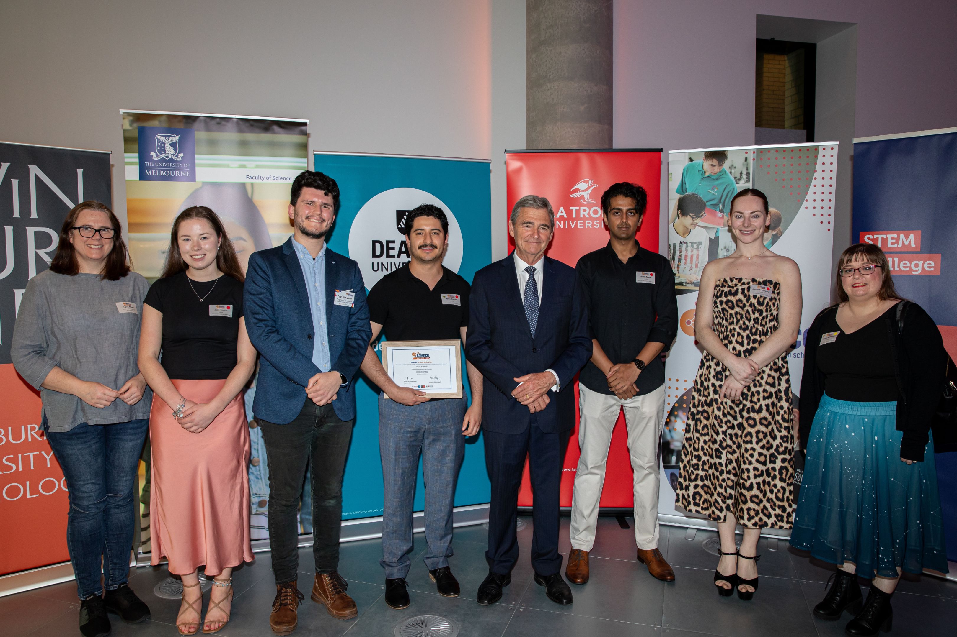 The Swinburne In2science team stand with the Hon John Brumby AO in front of various university branding