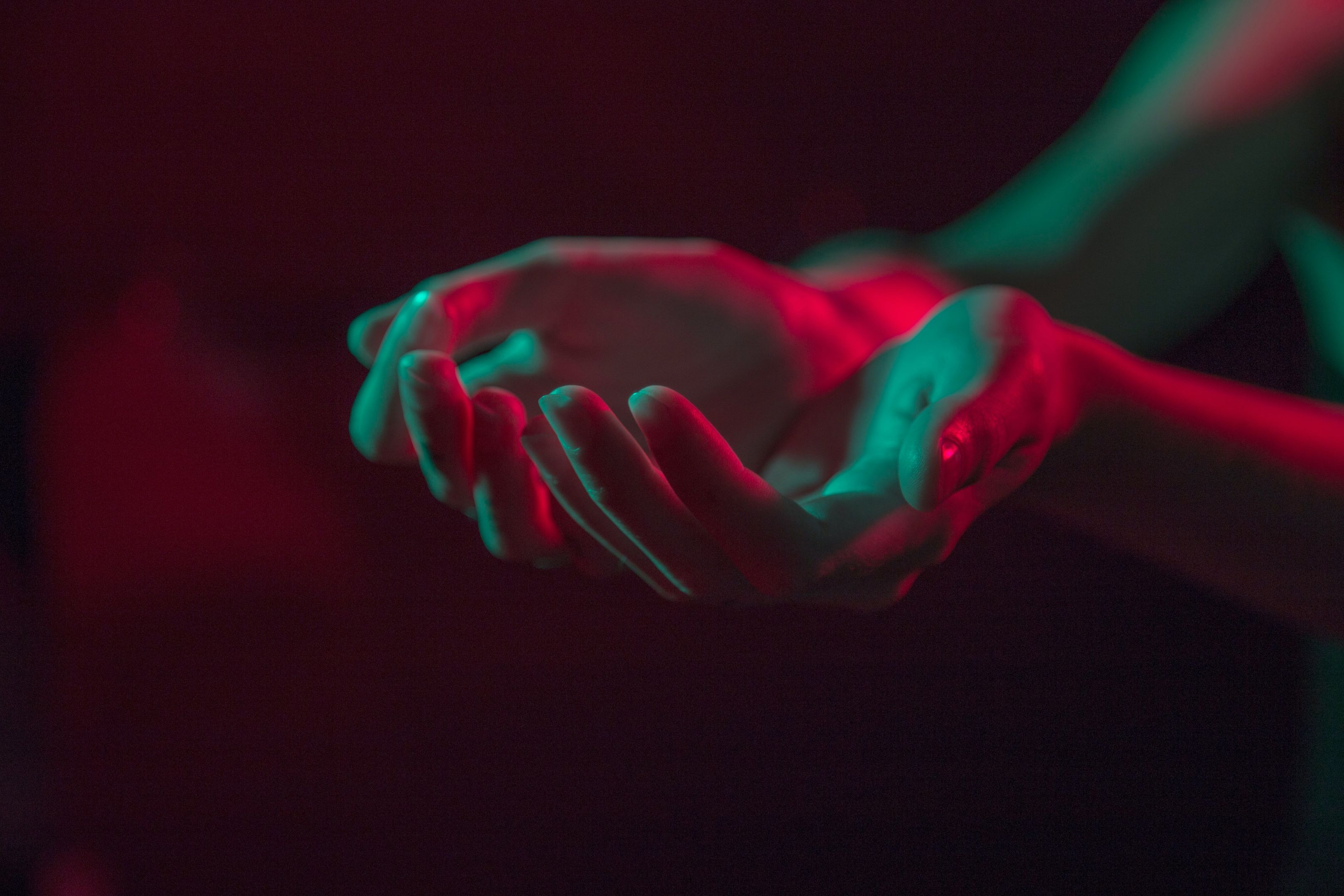 A pair of hands, open, ready to receive something are illuminated by red neon light giving the image a human yet futuristic feel. 