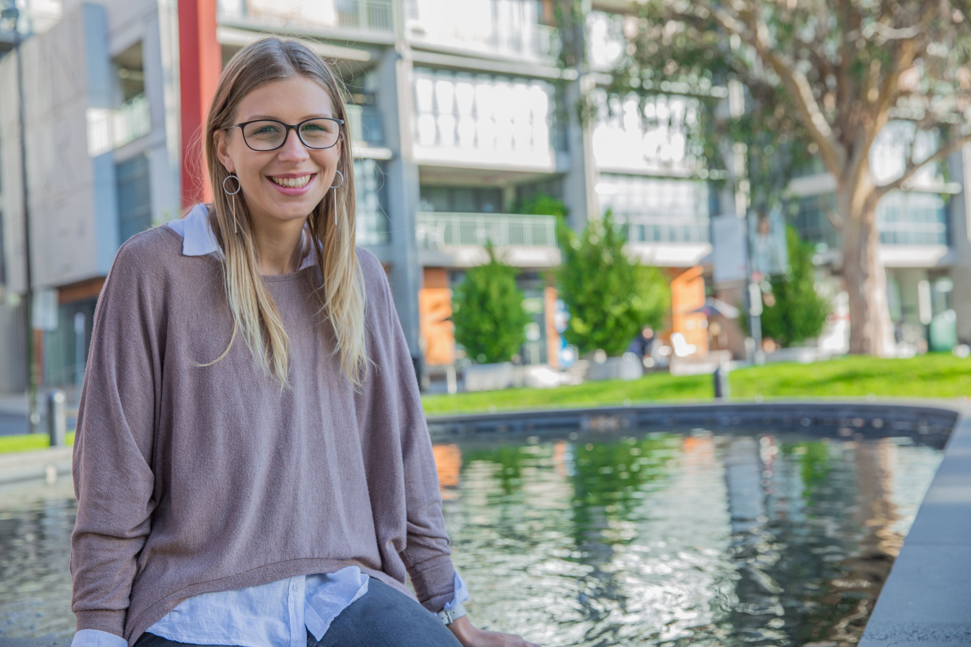 Swinburne student, Sally, sitting outdoors in front of a water fountain for her work placement. at Swinburne Abroad.