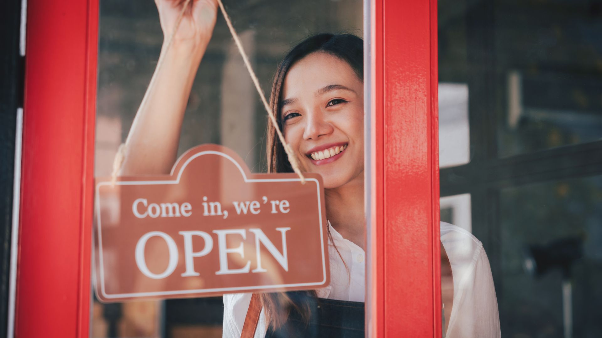 A female student wearing an apron opening a cafe door.