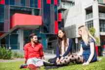 Three students sit outside in the Hawhtorn campus gardens, one male wears a red shirt