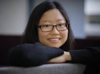 Zhou fang a student with her arms crossed on a couch looking at the camera smiling 