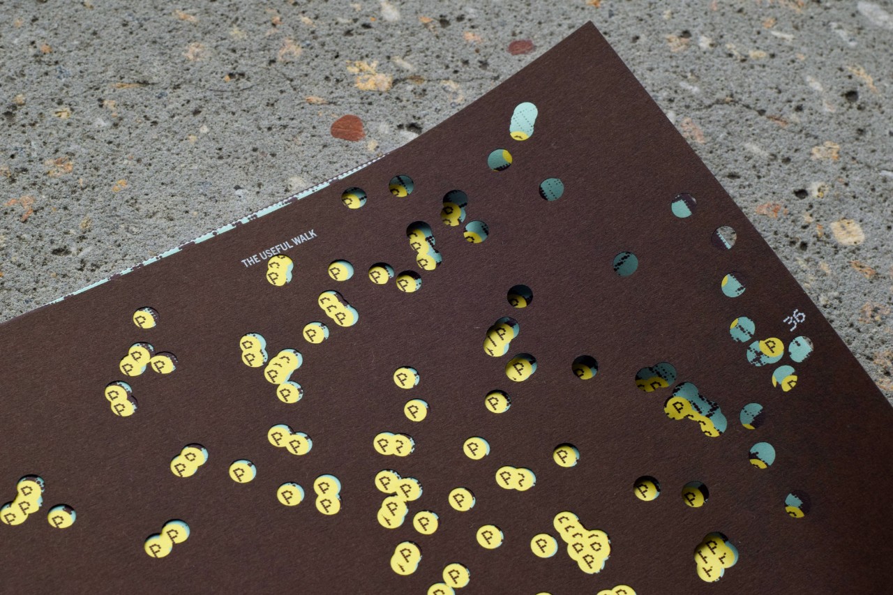 A black page full of holes reveals clusters of yellow dots on a page beneath.