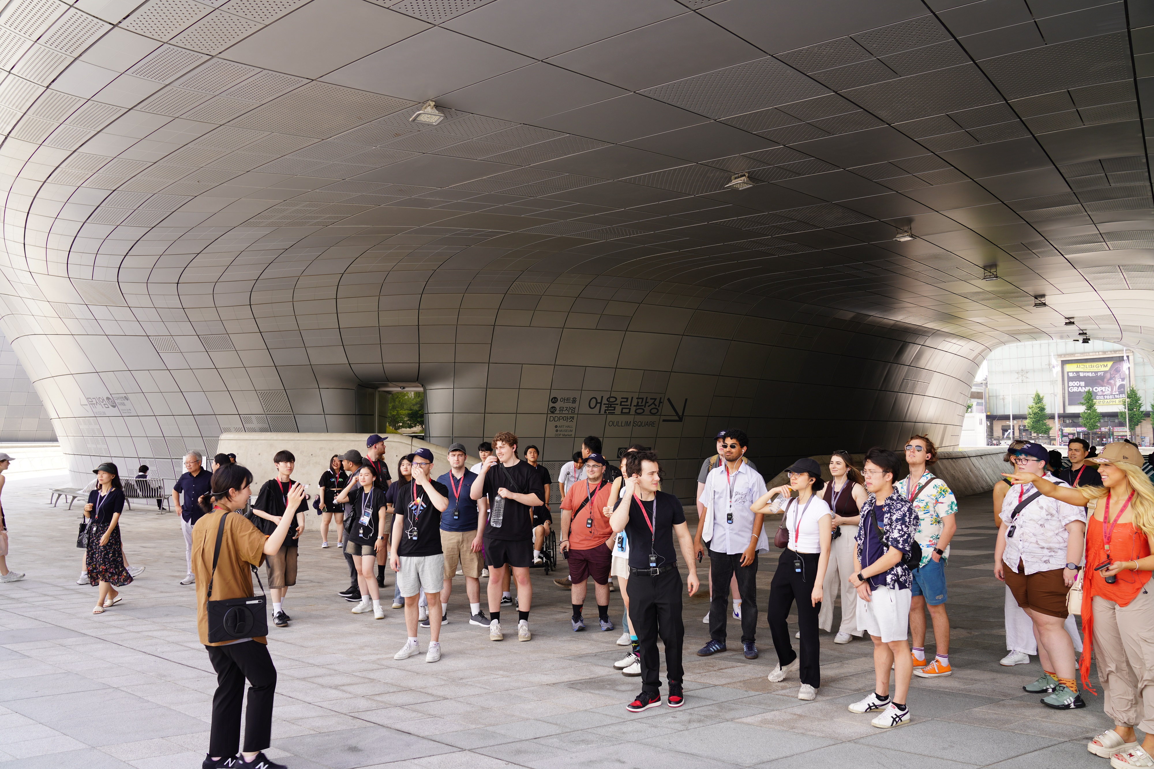 A group of students stand around outside beneath a futuristic silver building 