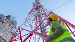 A female engineer in protective gear standing at the base of a telecommunications tower looking up