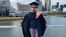 An image of a male student in graduation clothing in front of the yarra river