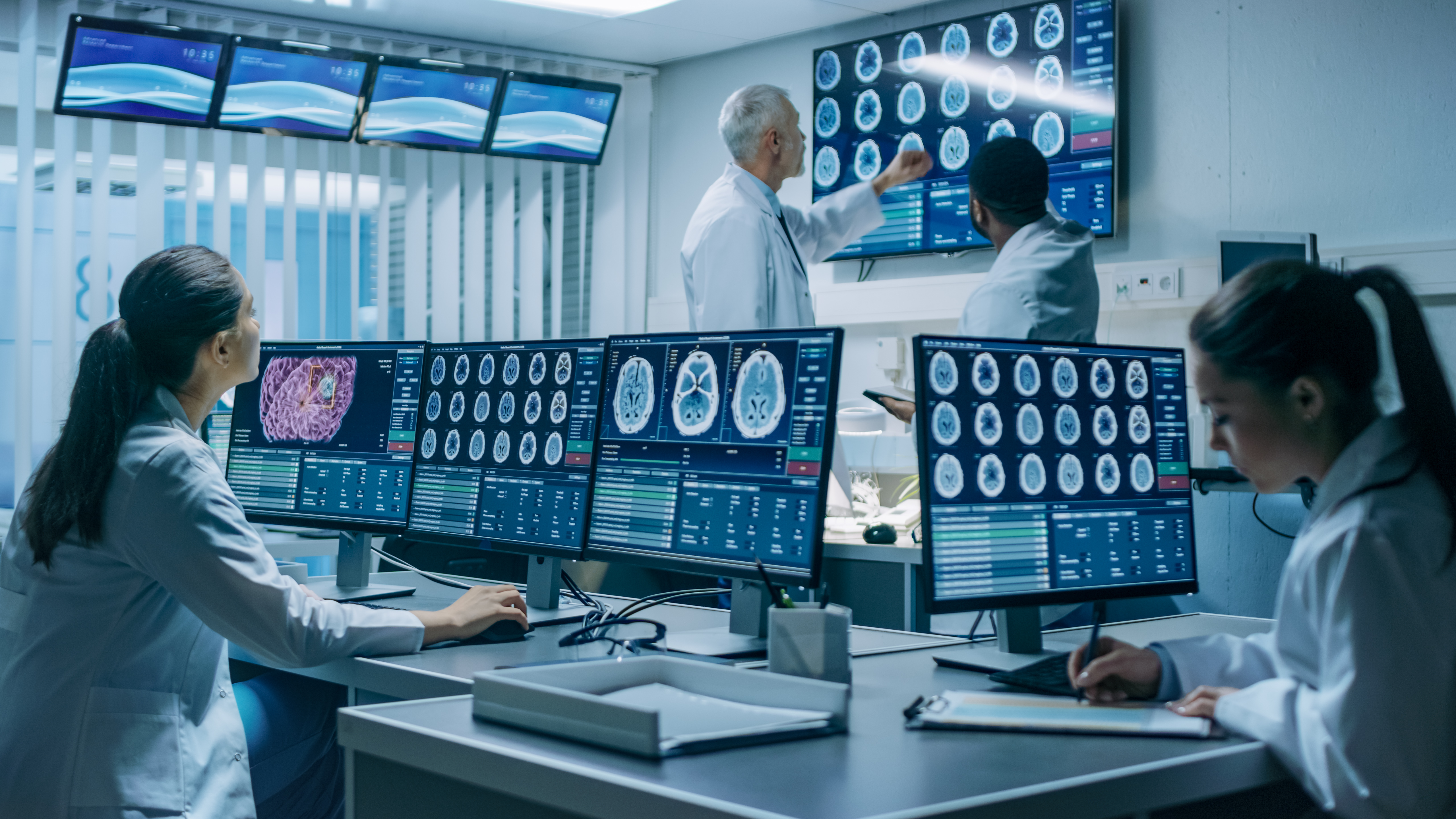 Neurologists / neuroscientists surrounded by monitors showing CT, MRI scans having discussions.