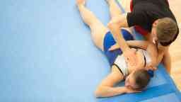 Sport Physio Therapist Helping Female Gymnast Stretching In Gym