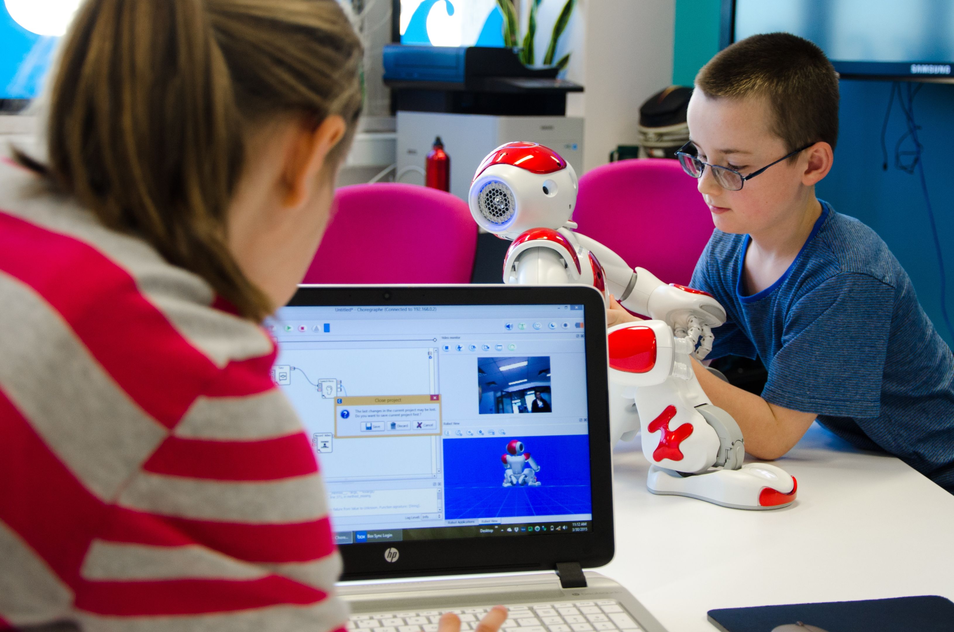 Woman looks at laptop while child plays with robot