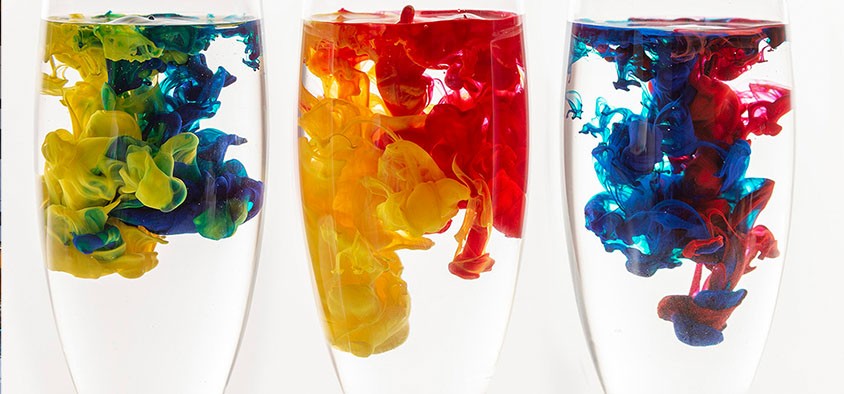 Photo of three champagne glasses filled with water and drops of coloured paint