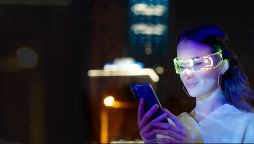 Young woman using smart phone in the city at night wearing glowing futuristic glasses.