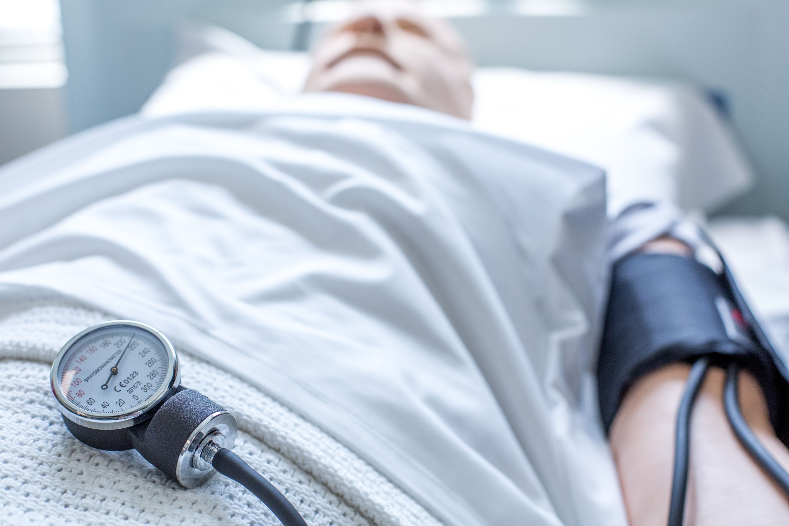 Dummy patient wearing white hospital gowns in blurred in the background and a sphygmomanometer sits in focus