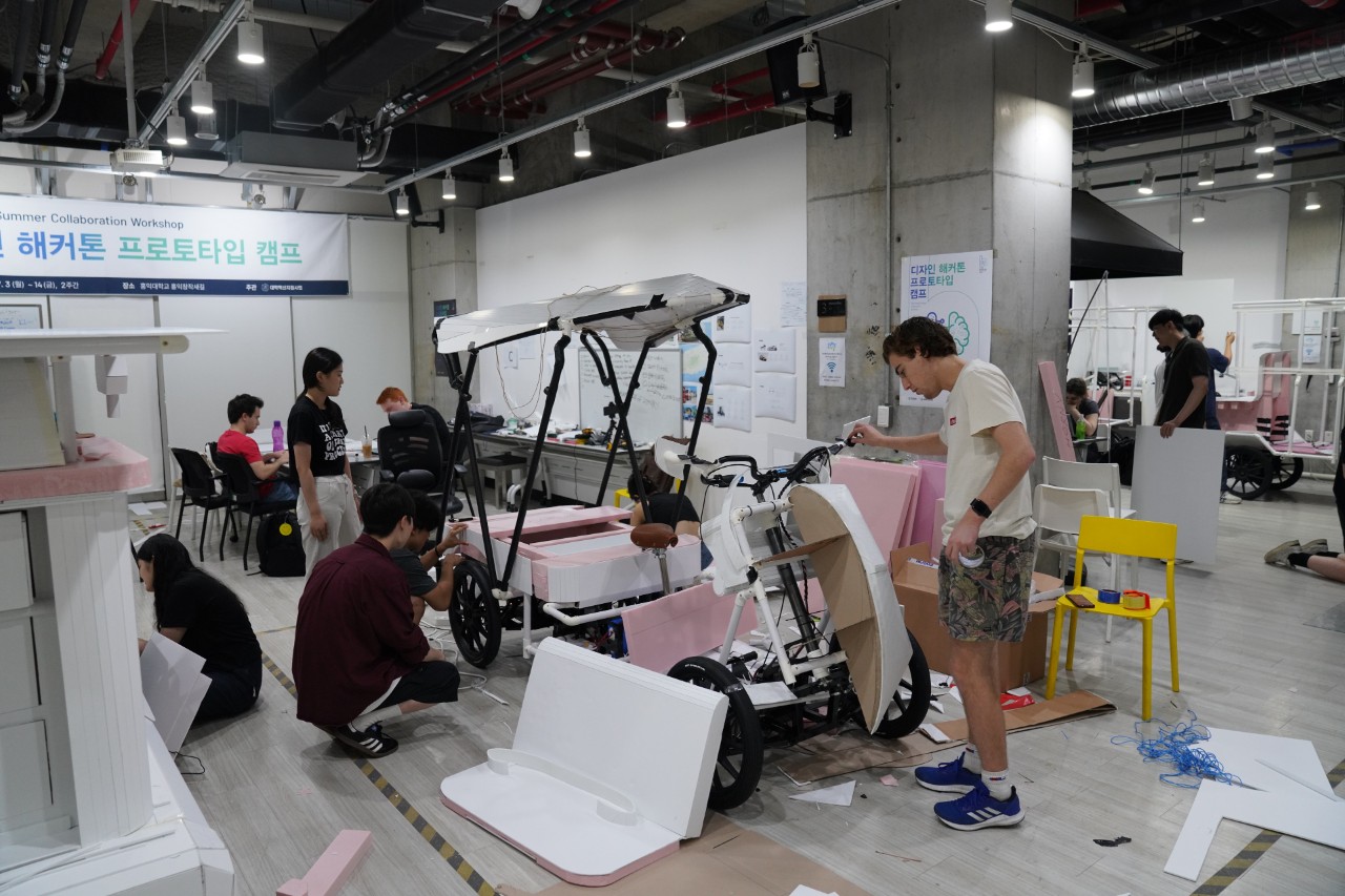 Students stand around a partially constructed prototype of a four-wheel mobility design, foam and card have been added to a metal fram